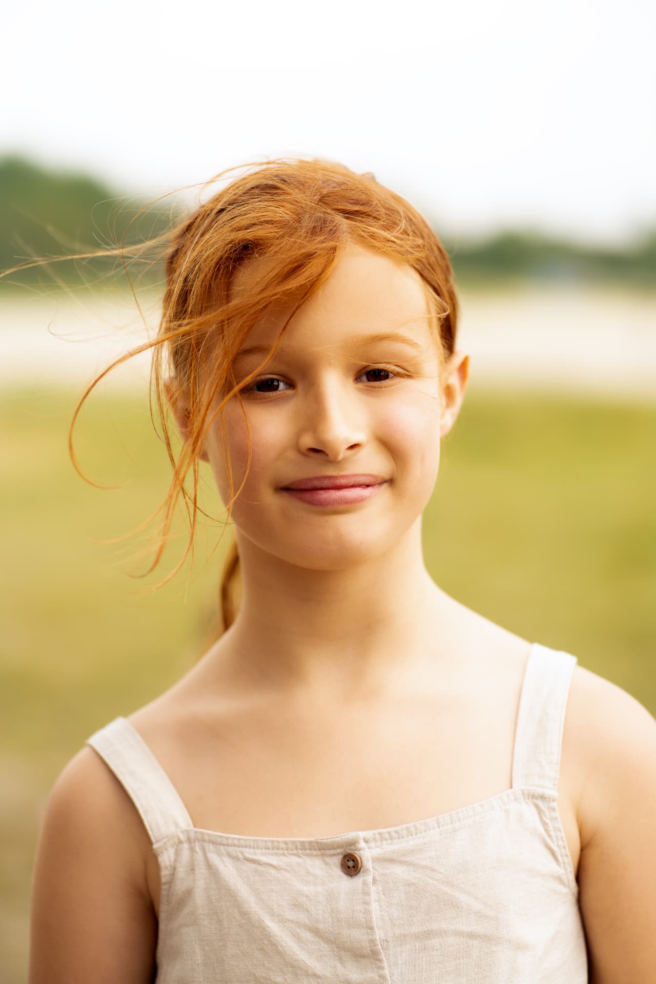 Close portrait of a red-haired girl with a kite, hair blown across her face in warm daylight