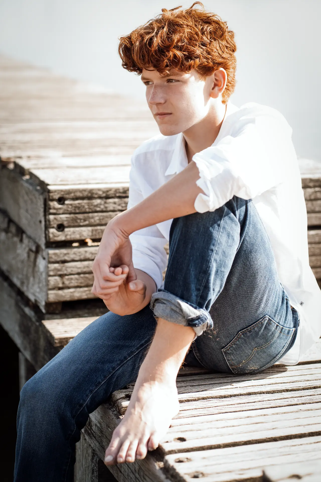 Shey seated barefoot on a sunlit wooden jetty