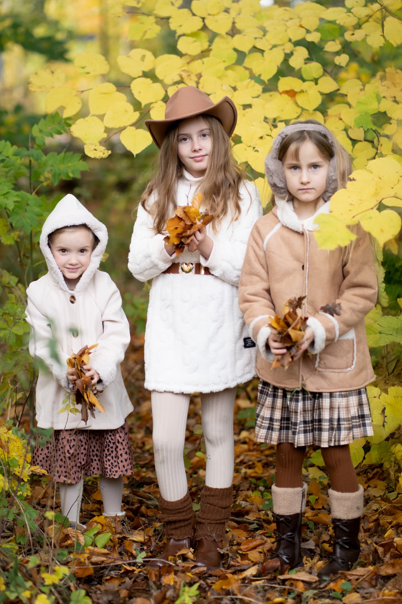 Three girls holding bouquets of autumn leaves among yellow foliage
