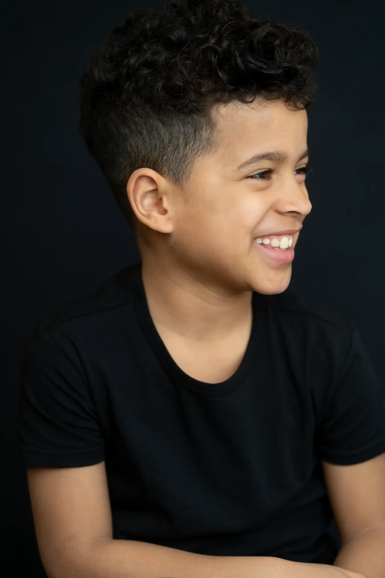 Smiling boy in black against a deep charcoal backdrop