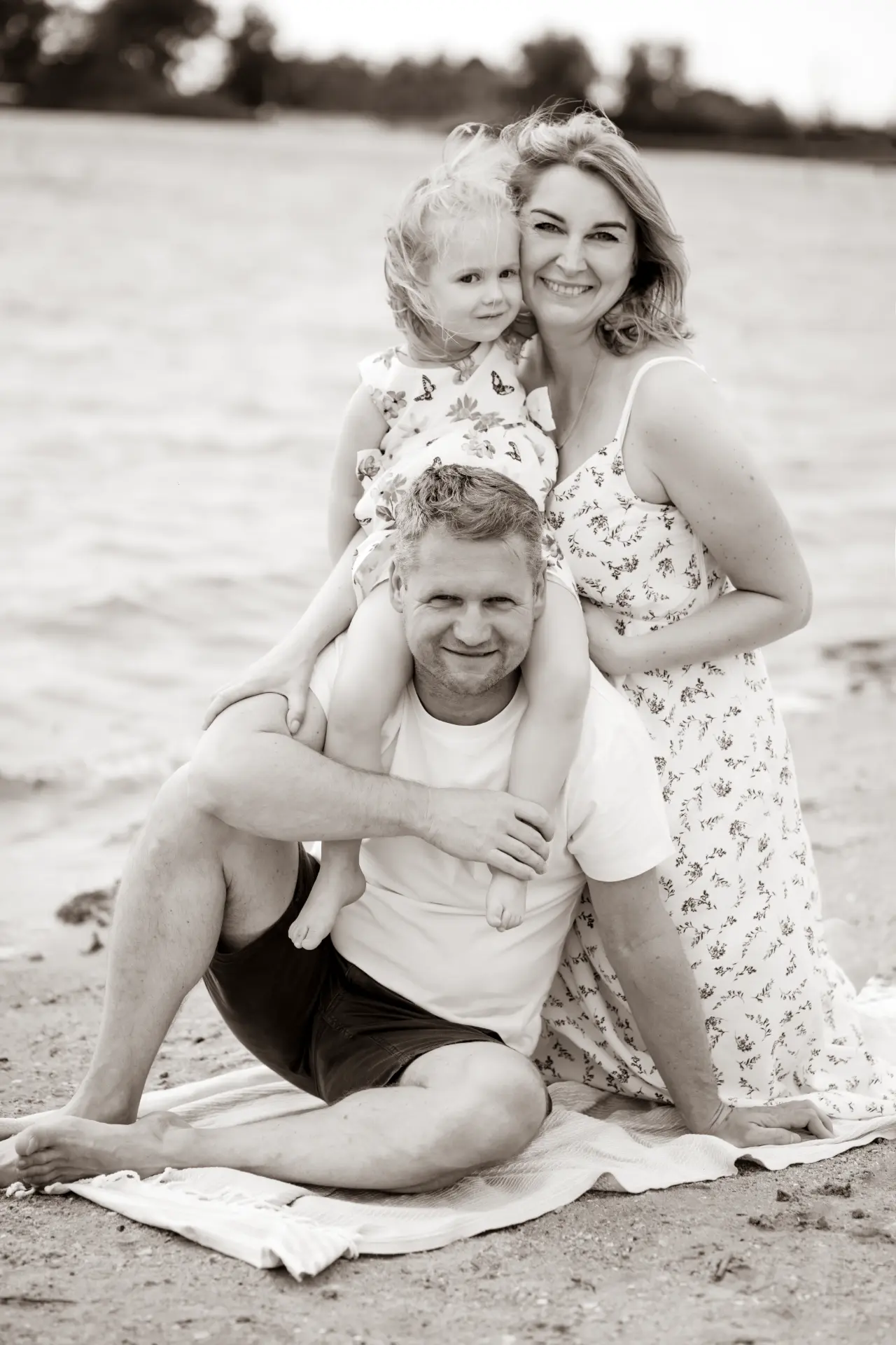 Black and white family portrait on the sand, daughter on her father's shoulders
