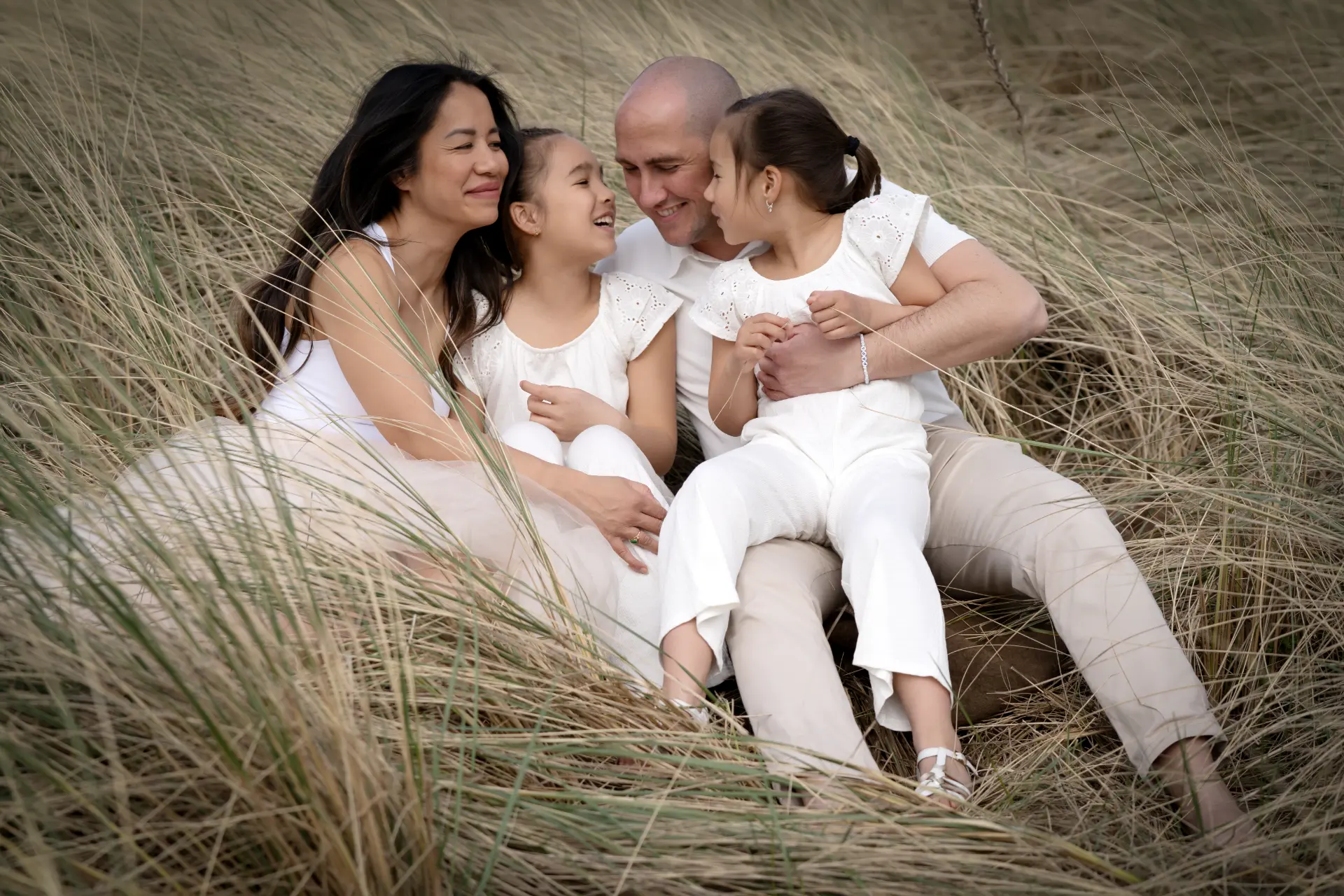 Family of four sitting together and laughing in tall dune grass