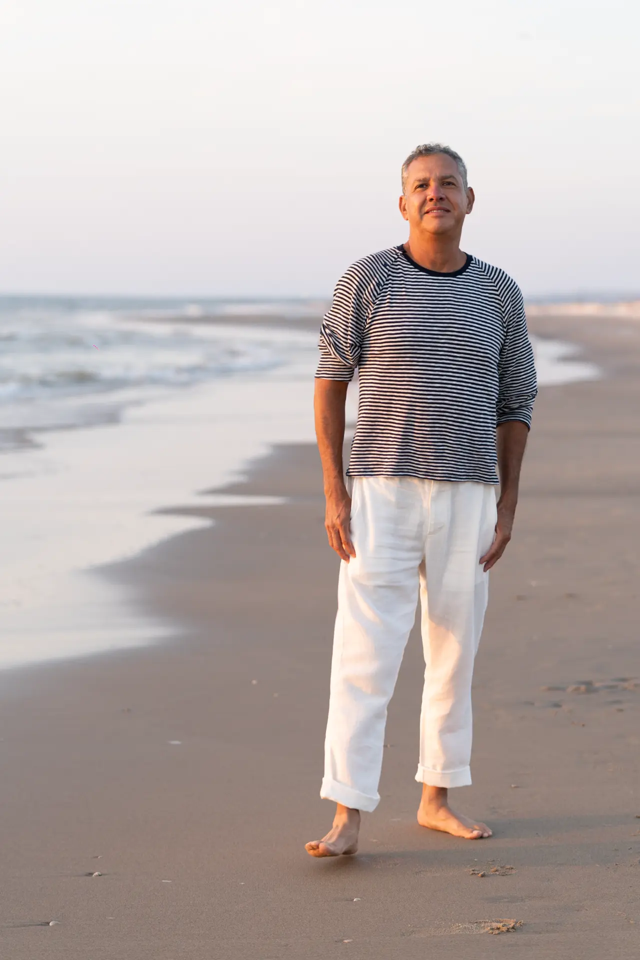 Rey standing barefoot on the beach in warm evening light