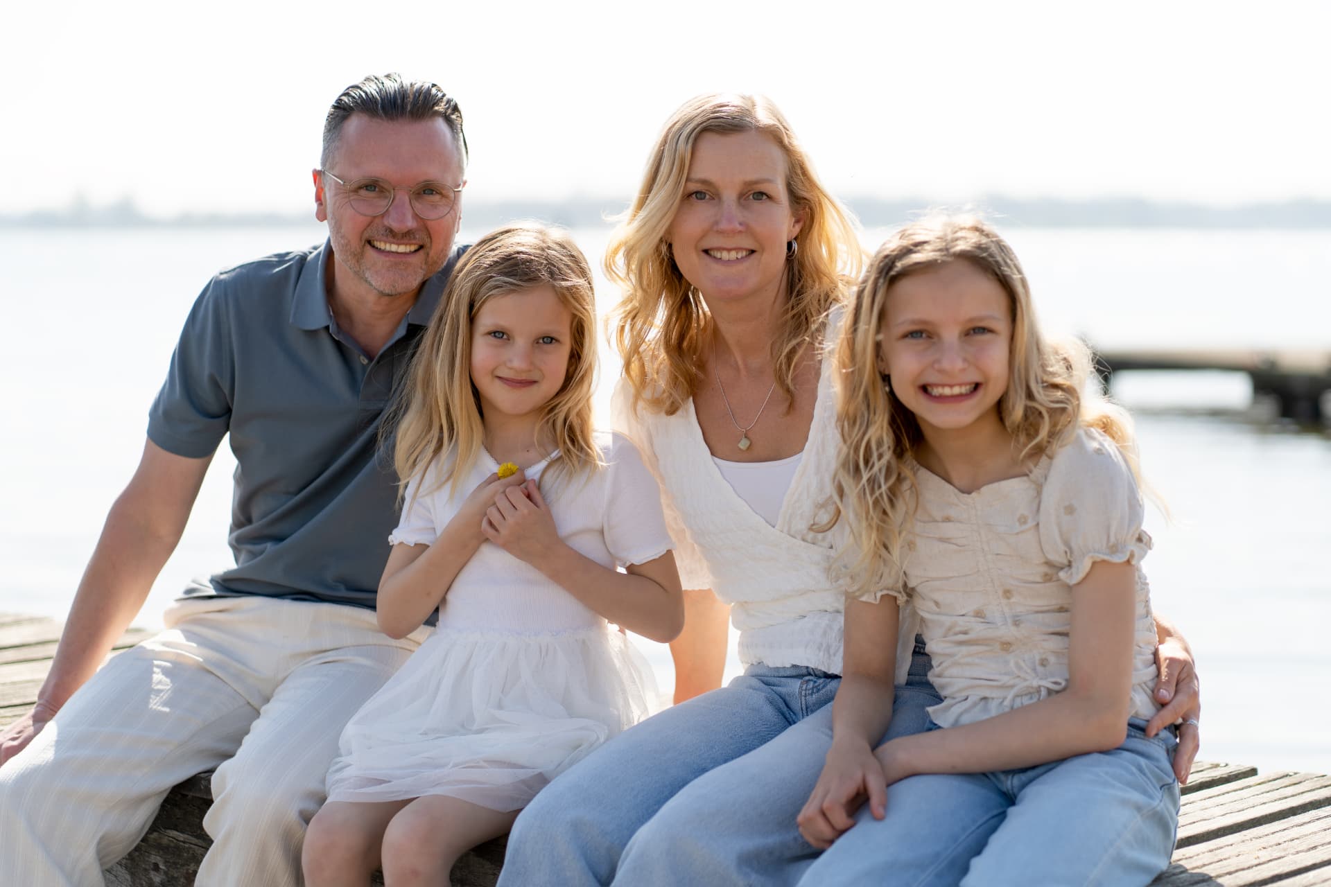 Family of four seated on the jetty against the bright water