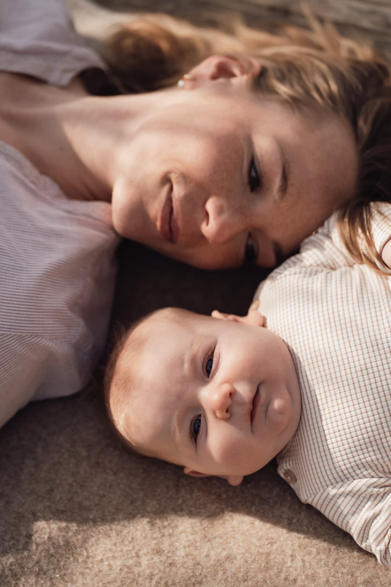 Close portrait of a mother and baby lying cheek to cheek in warm light