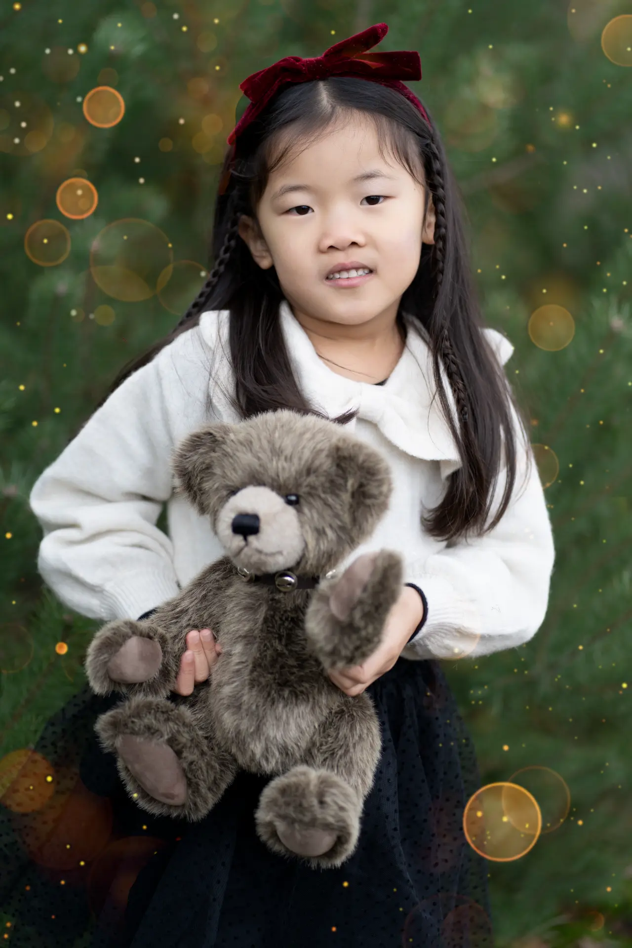 Girl holding her teddy bear among glowing Christmas lights