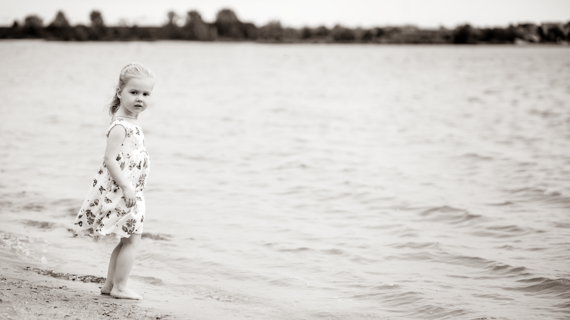 Girl in a floral dress standing barefoot at the water's edge