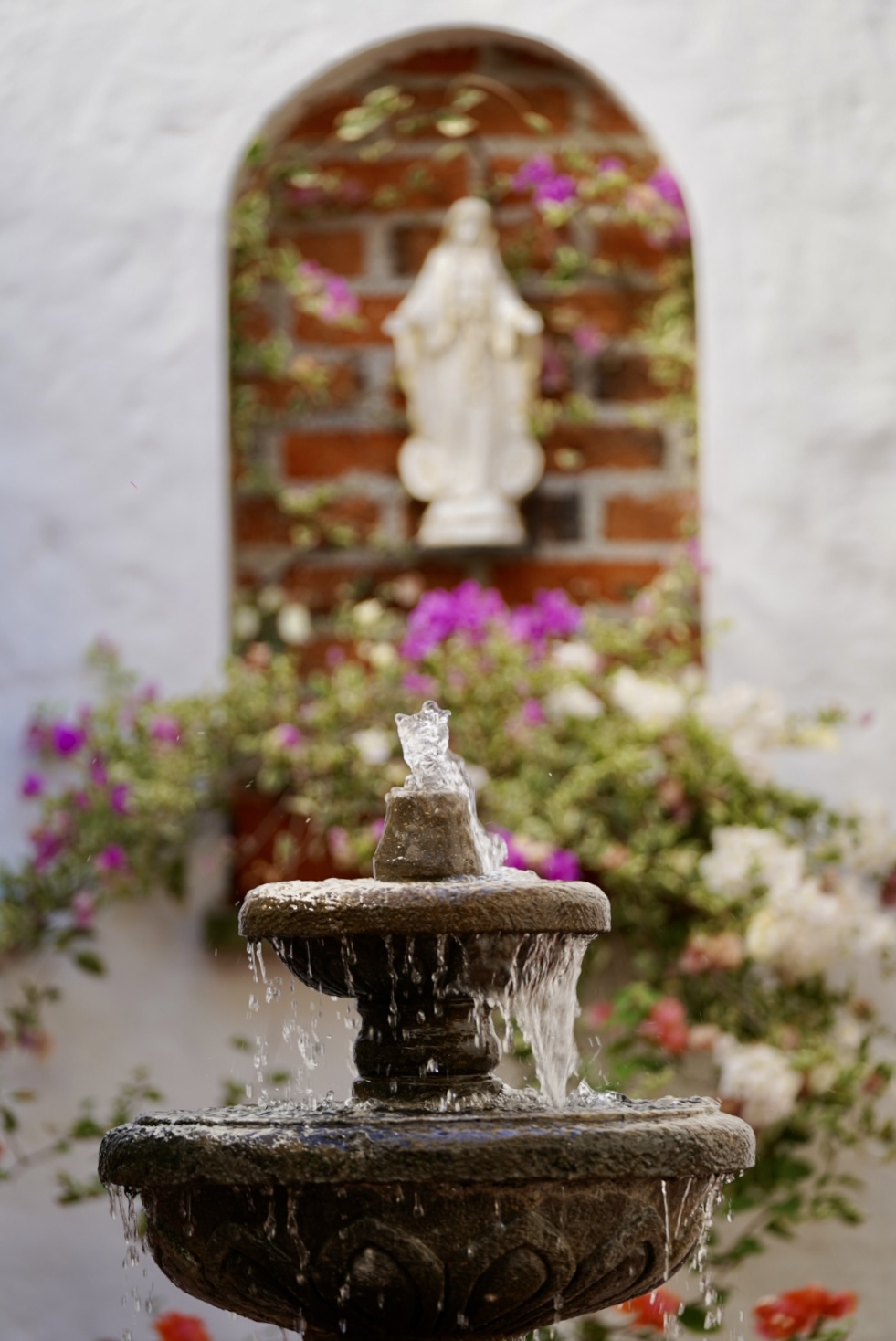 Water spilling from the courtyard fountain below an alcove of flowers