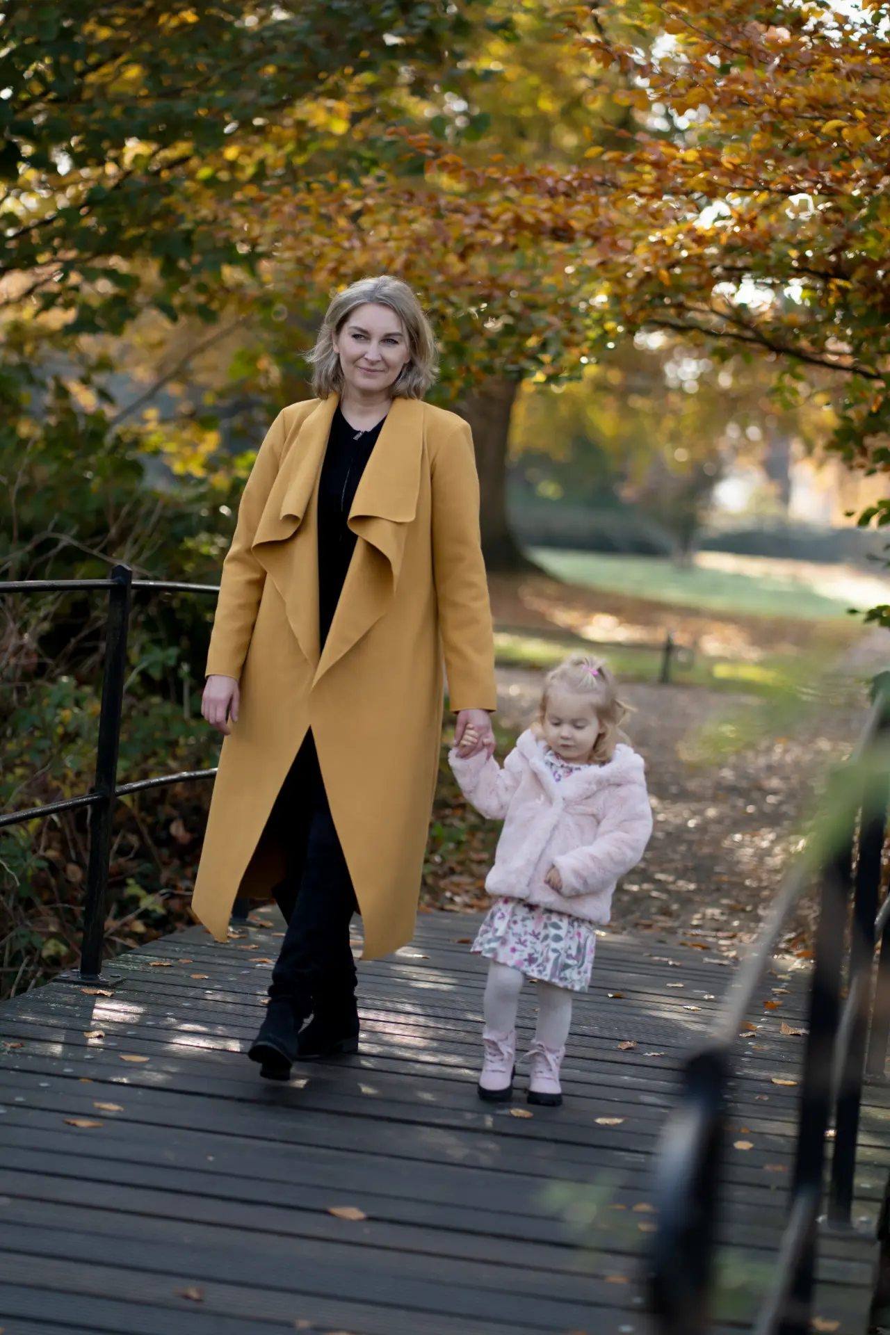 Mother and daughter walking hand in hand across a woodland bridge
