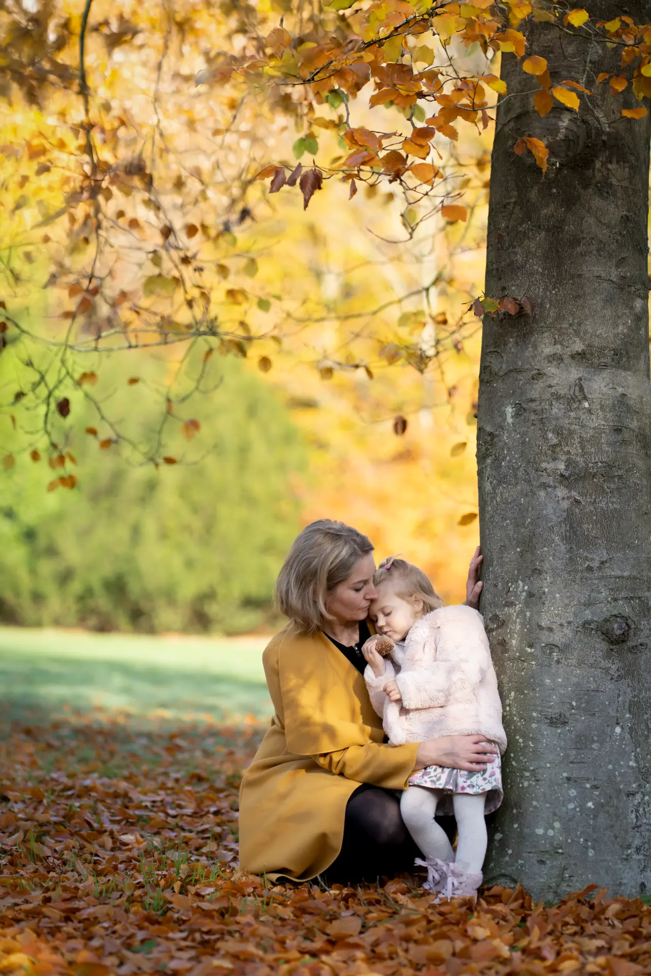 Mother embracing her daughter beneath a golden autumn tree