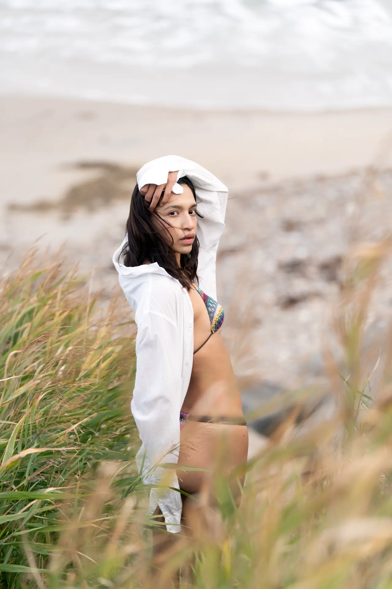 Woman shading her eyes in tall grass by the sea