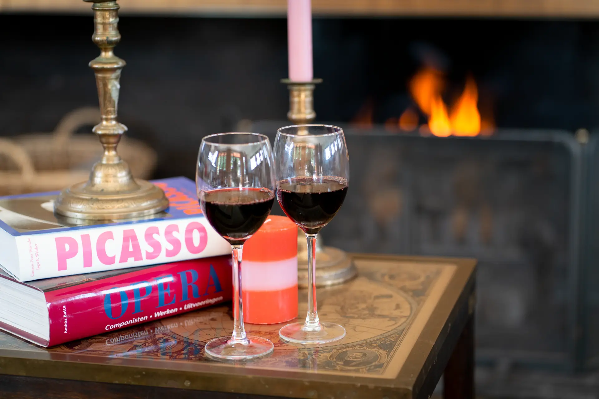 Two glasses of red wine and a striped candle on the table, the fire glowing behind