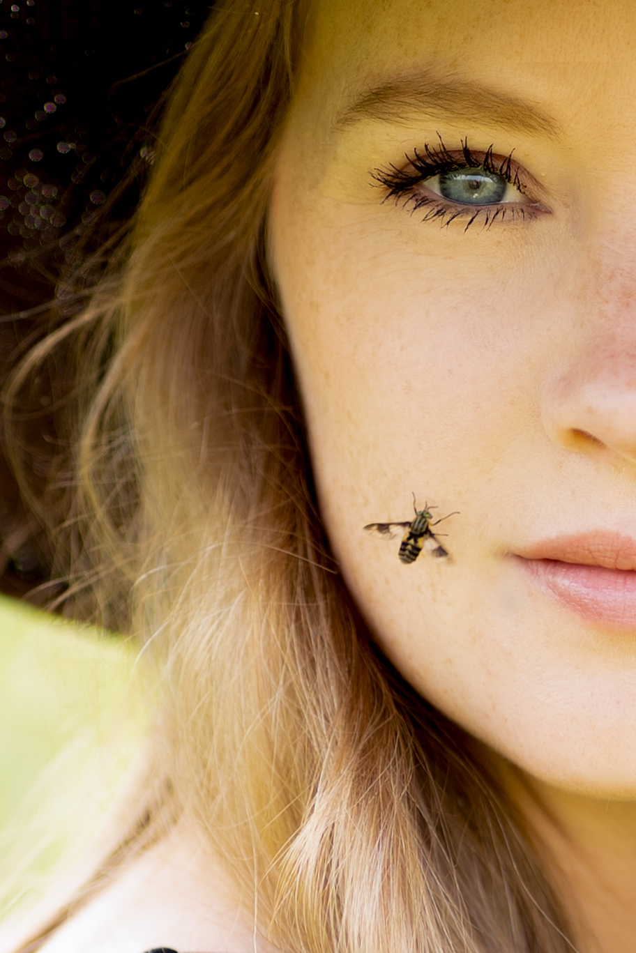 Close crop of a woman's face in golden light with an insect resting on her cheek