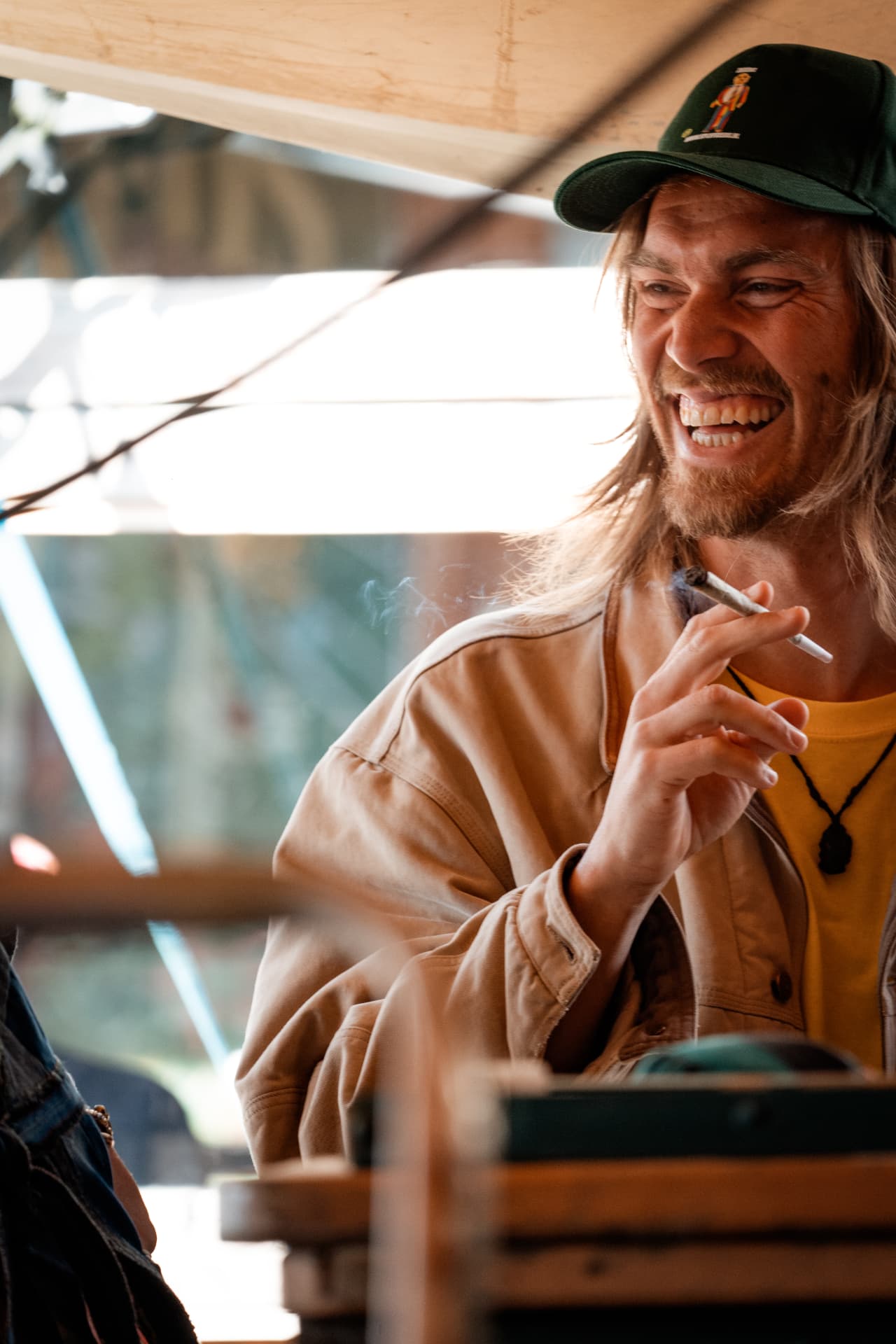 Laughing guest in a dark cap sharing a smoke
