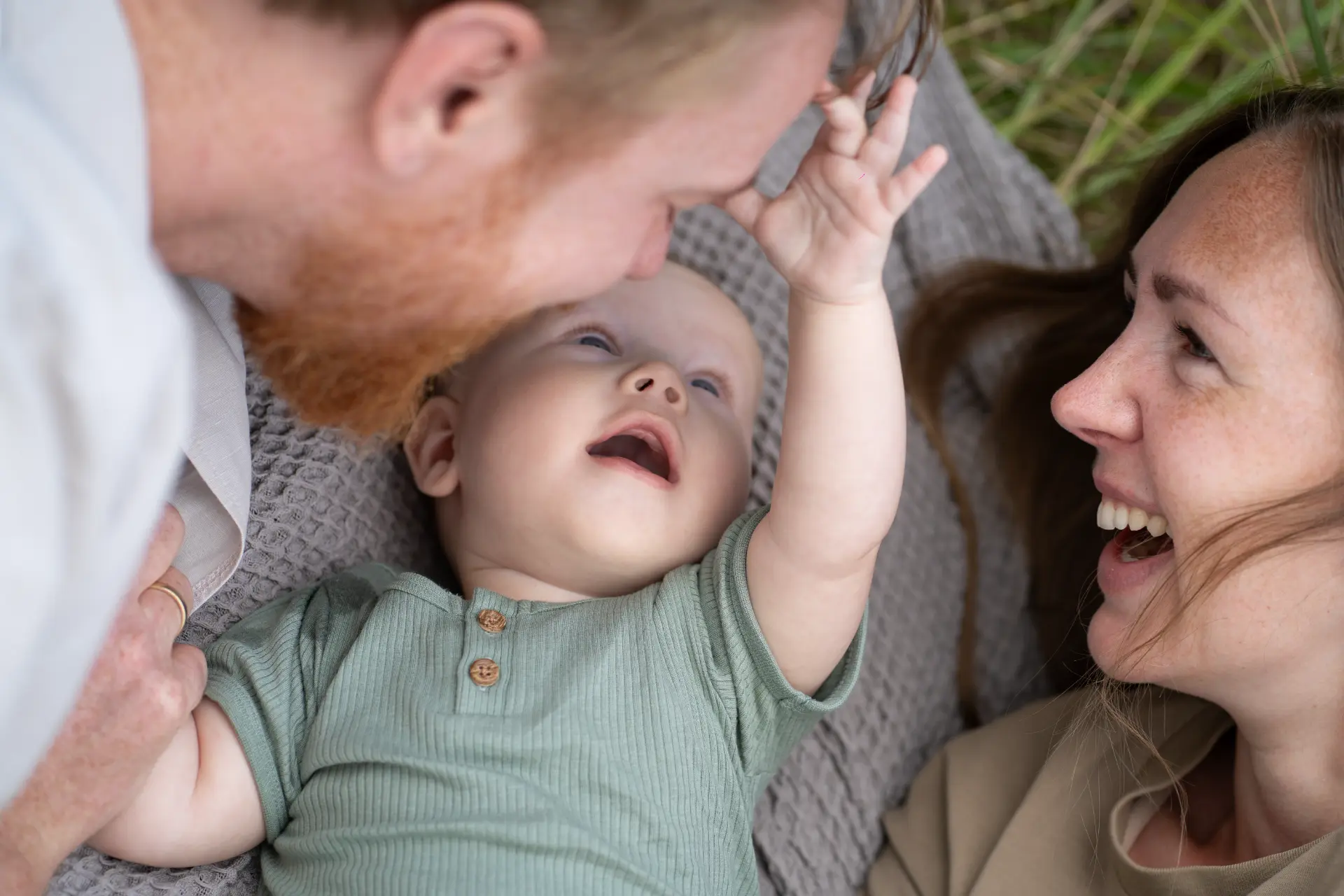 Parents lying either side of their laughing baby on a blanket