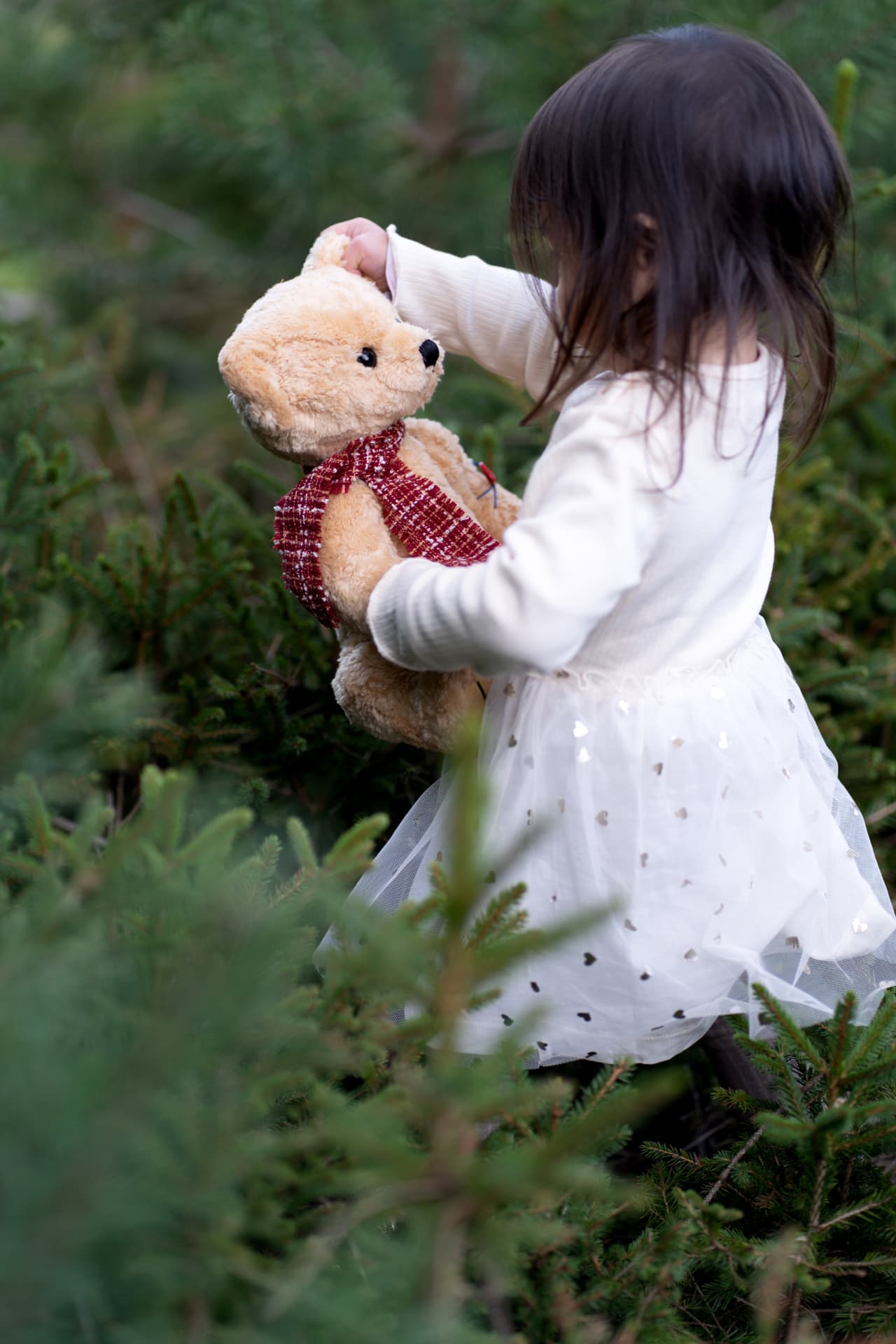 Little girl carrying her teddy bear through the trees
