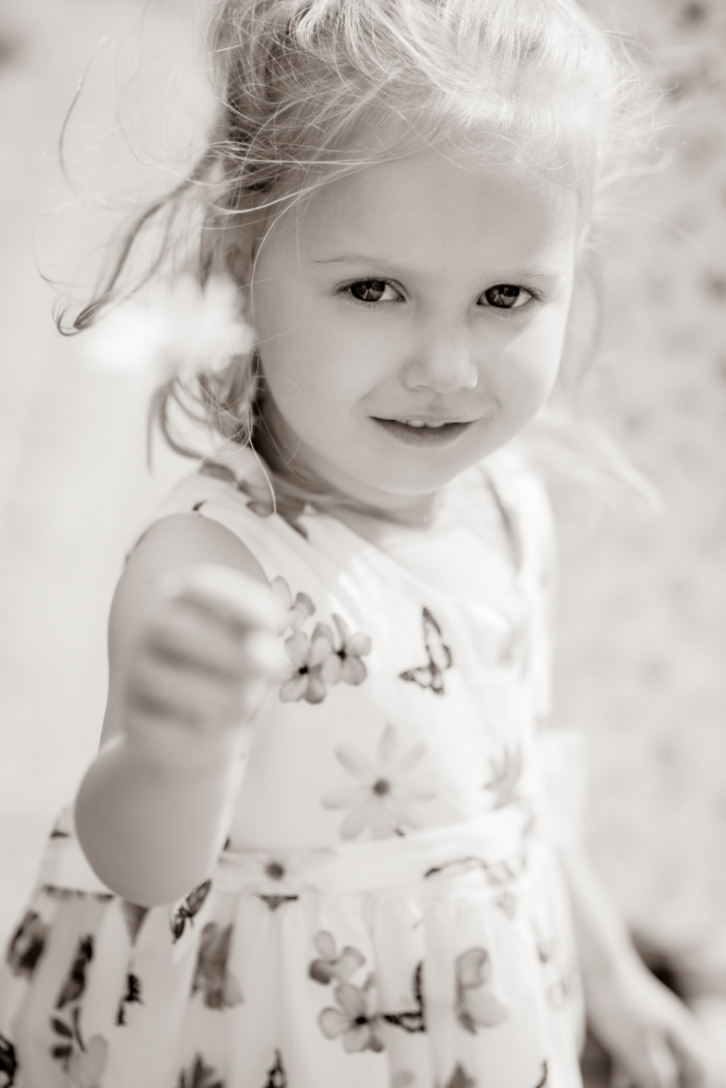 Close black and white portrait of a girl holding out a small flower