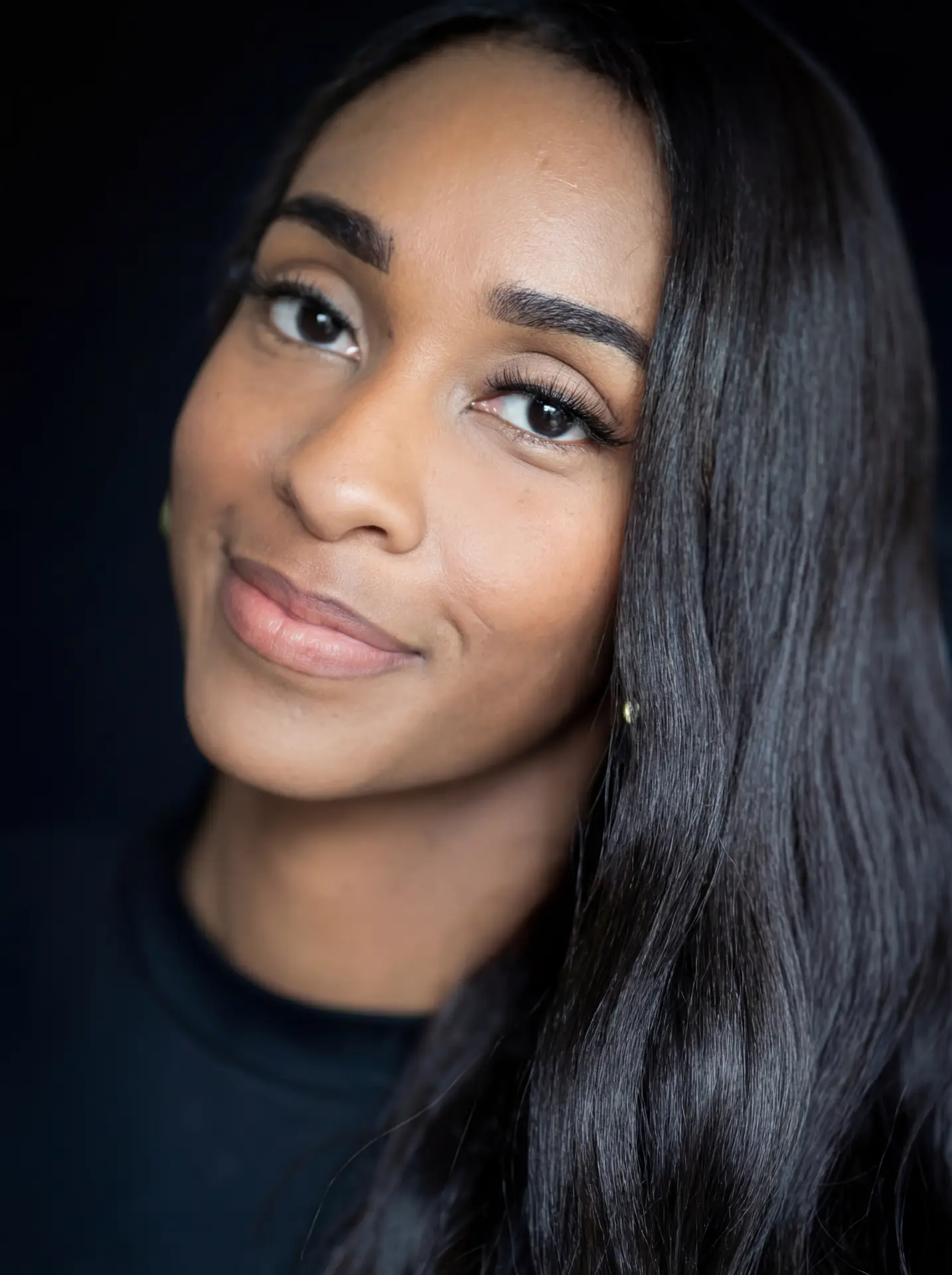 Woman with long dark hair against a dark backdrop