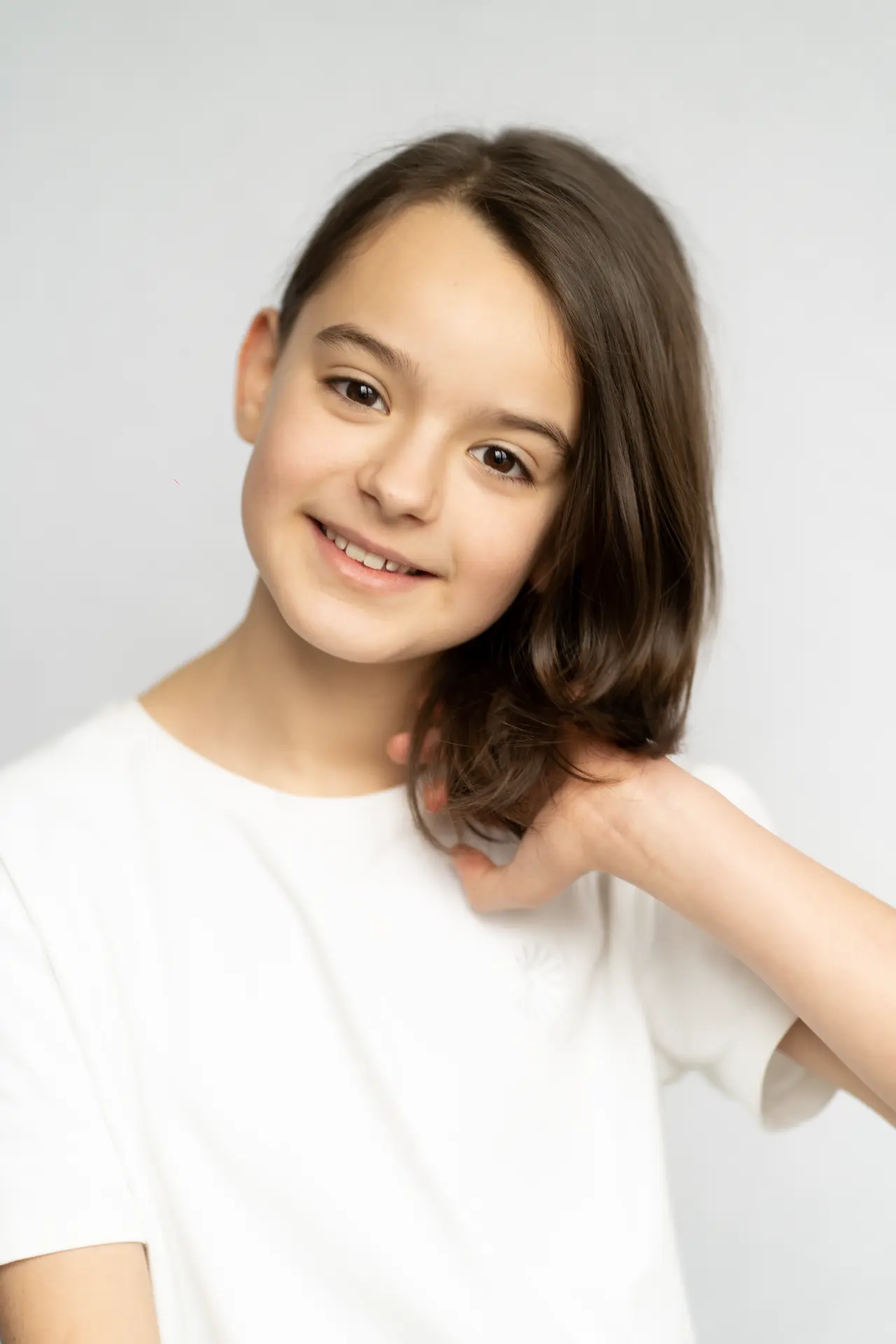 Girl in a white shirt tucking her hair back in a light studio