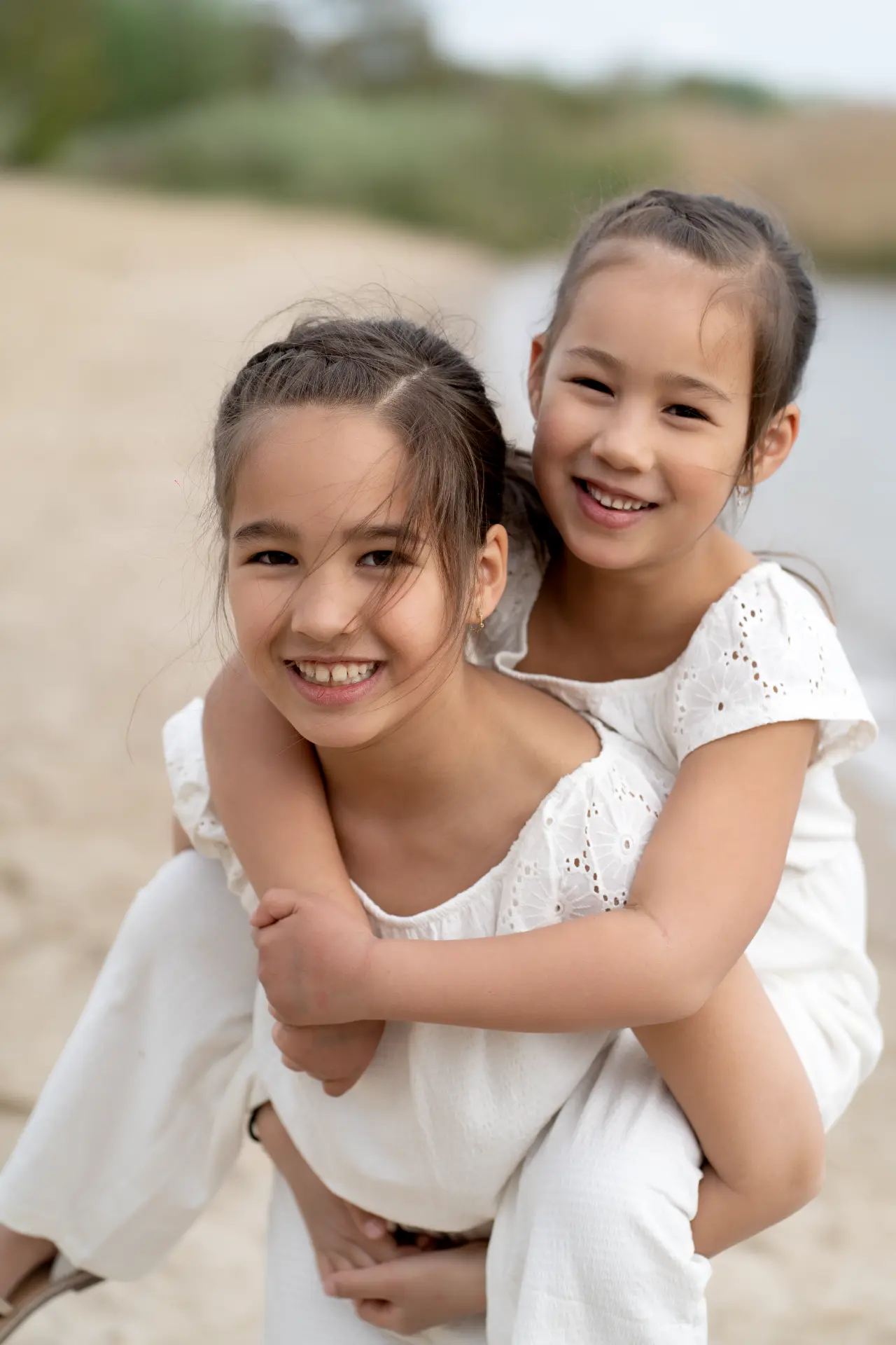 One sister carrying the other on her back on the sand