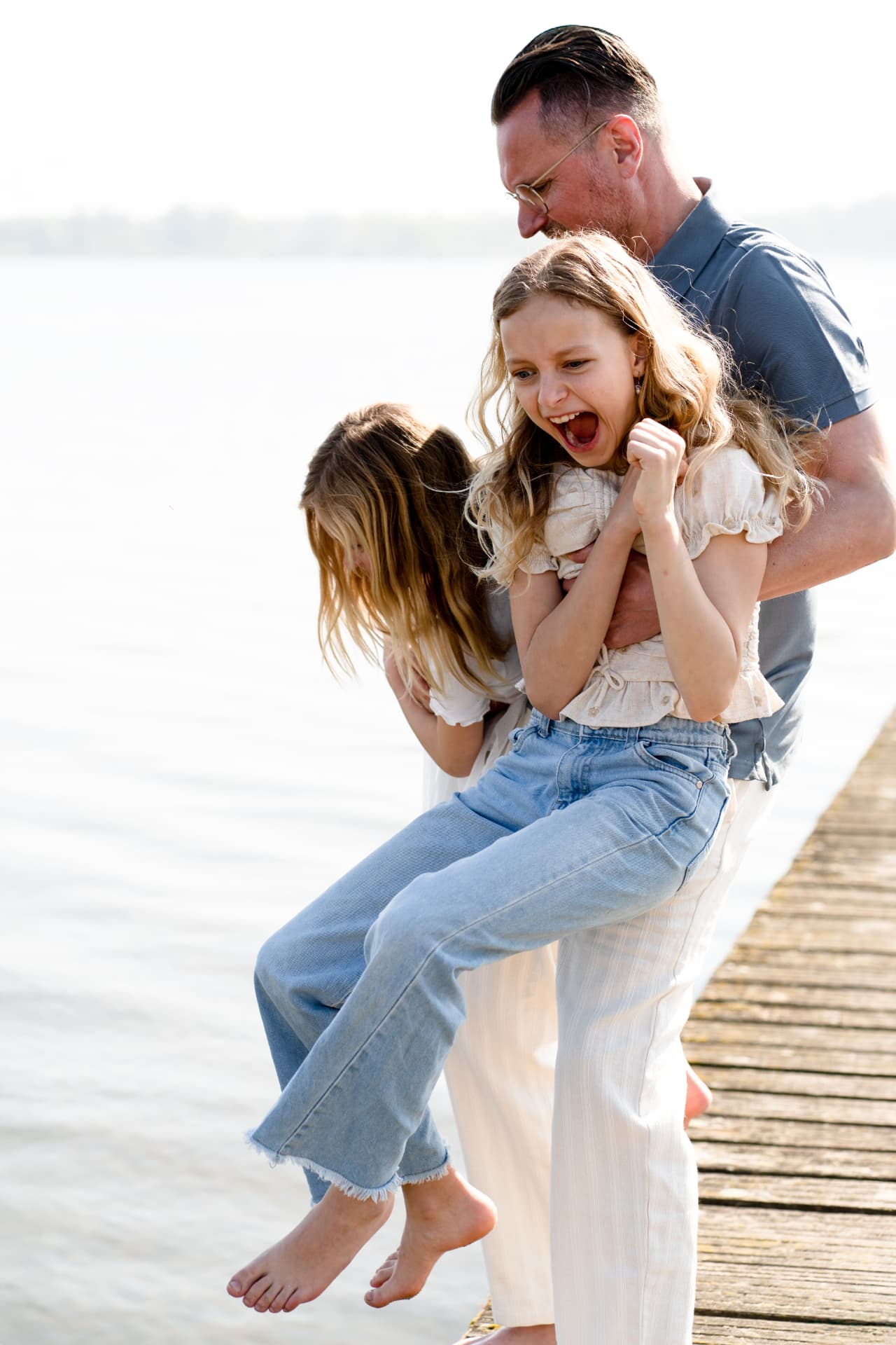 Father lifting his two daughters on the jetty as they laugh