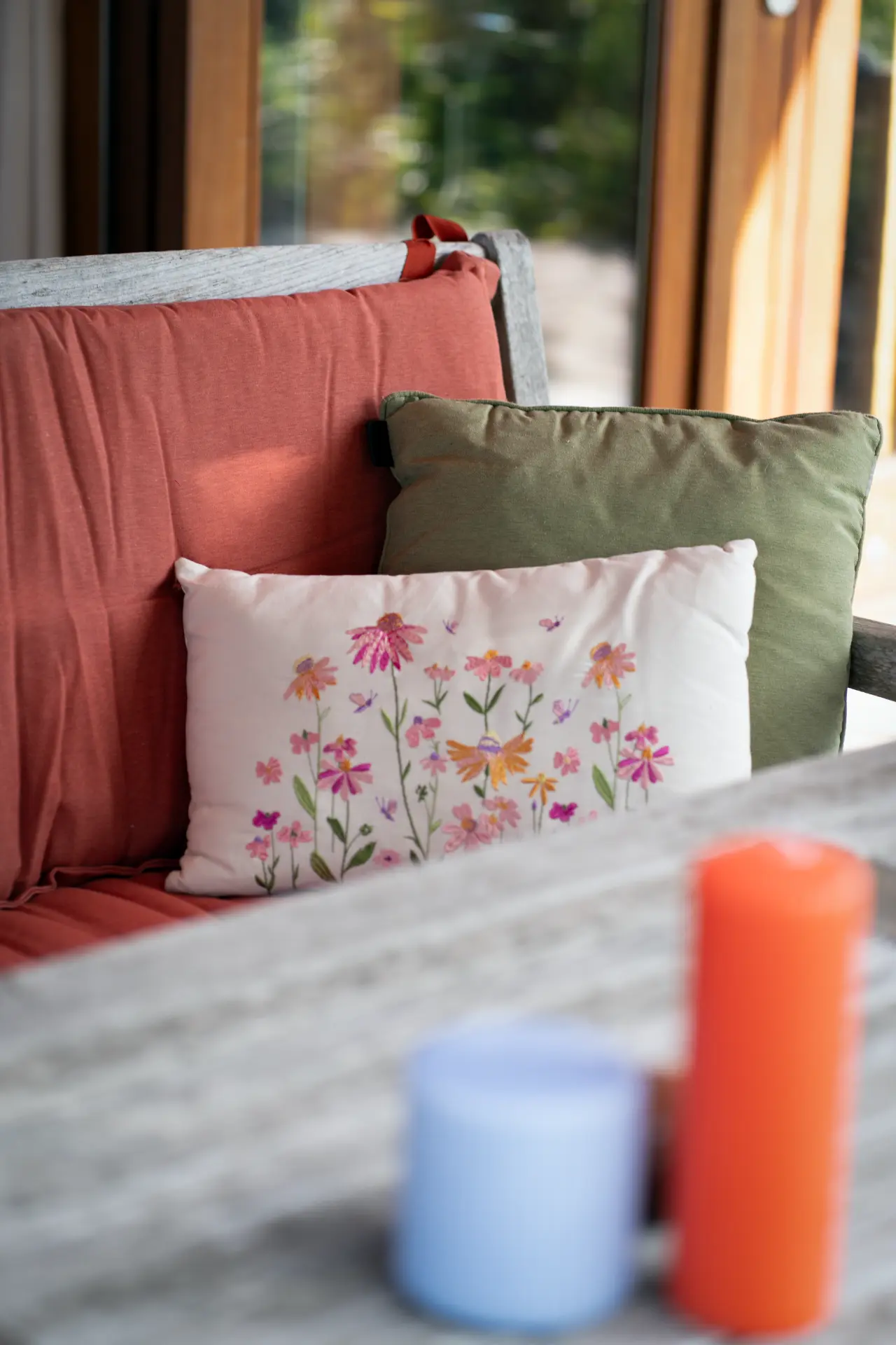 Coral and sage cushions with an embroidered white pillow on the garden bench