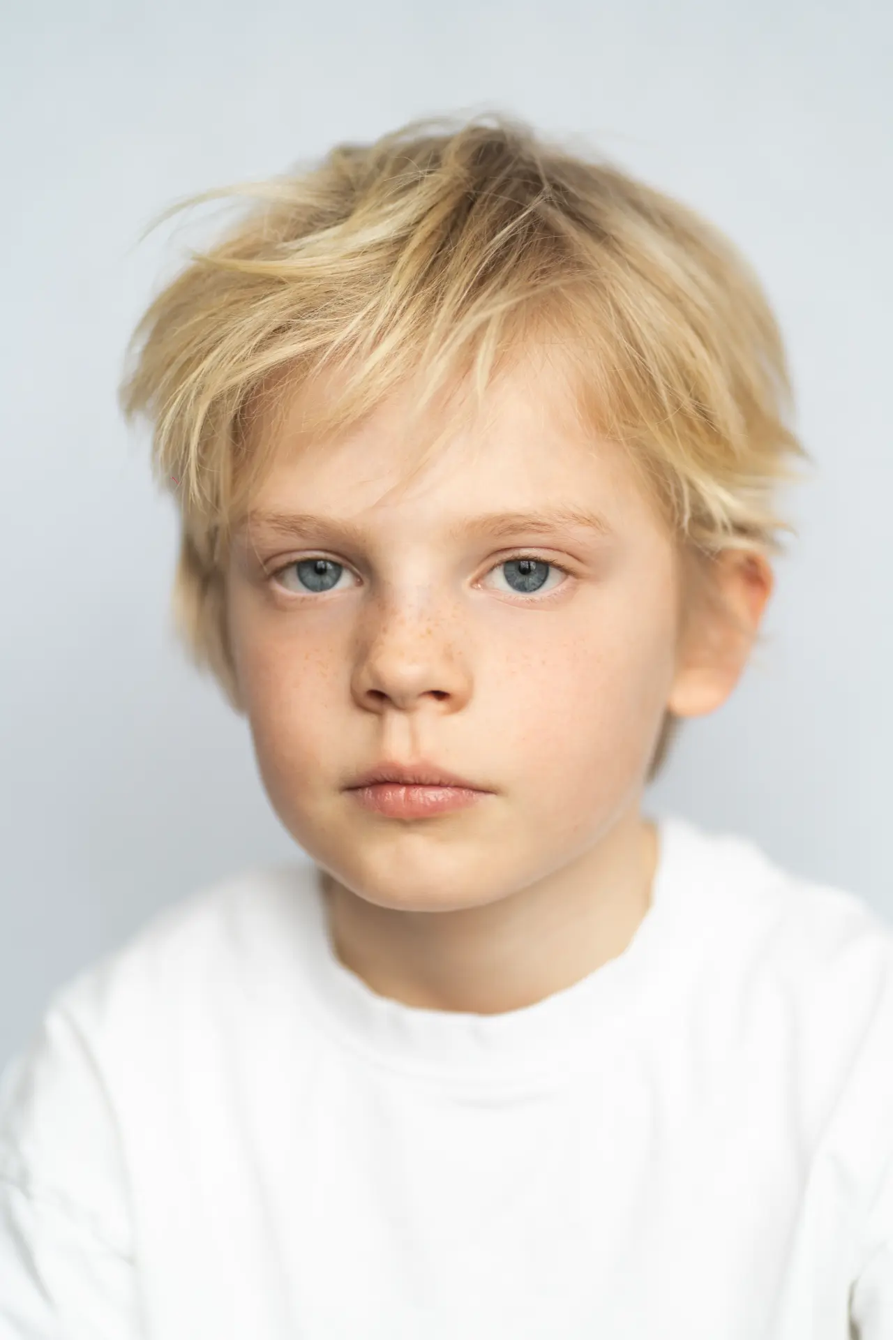 Blond boy looking straight into the camera in a white studio