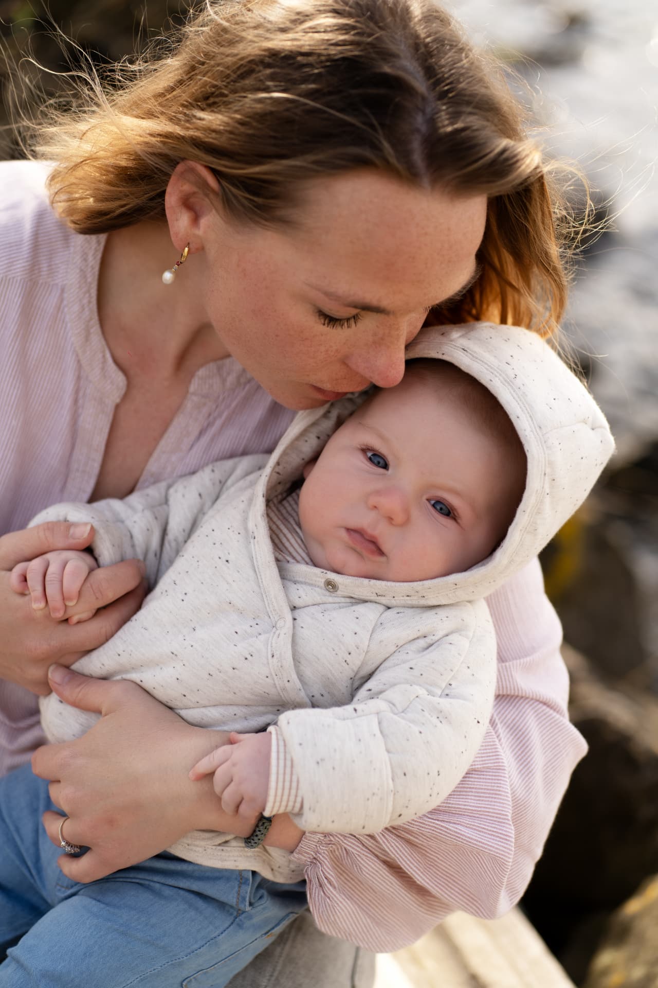 Mother resting her head against her baby in a hooded suit in golden light
