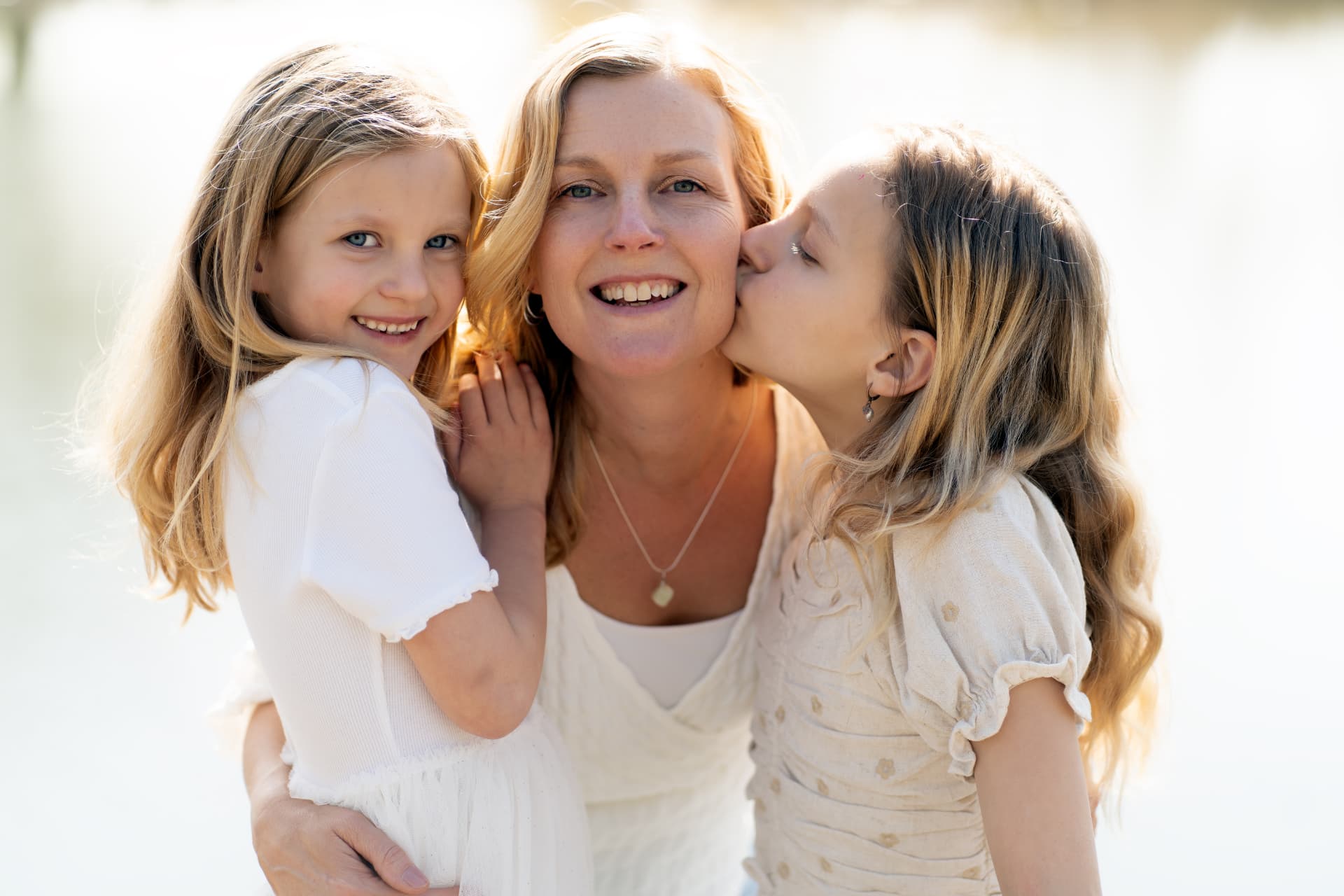 Mother laughing while her daughters kiss and hug her