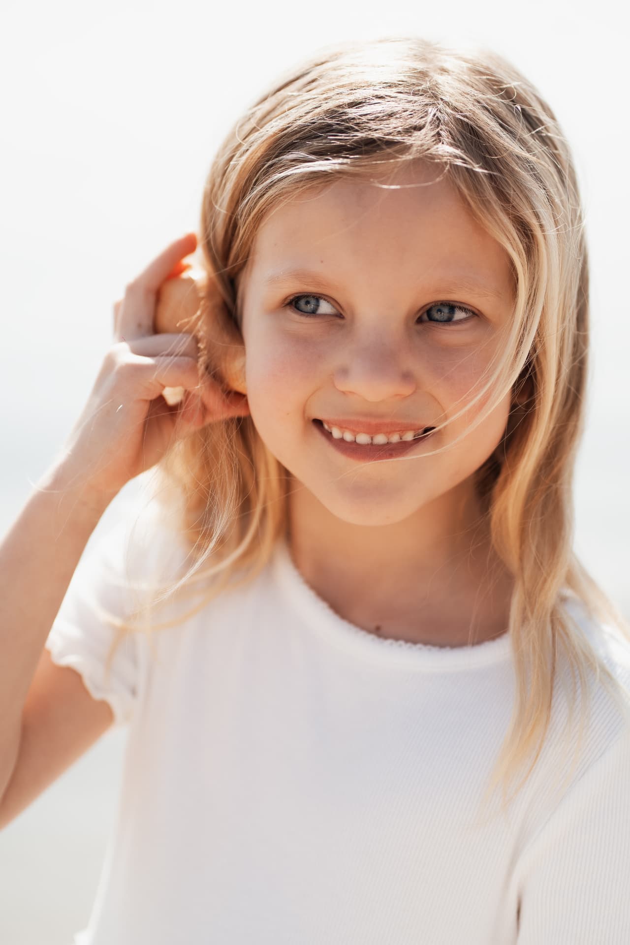 Girl in white listening to a shell, smiling in bright light