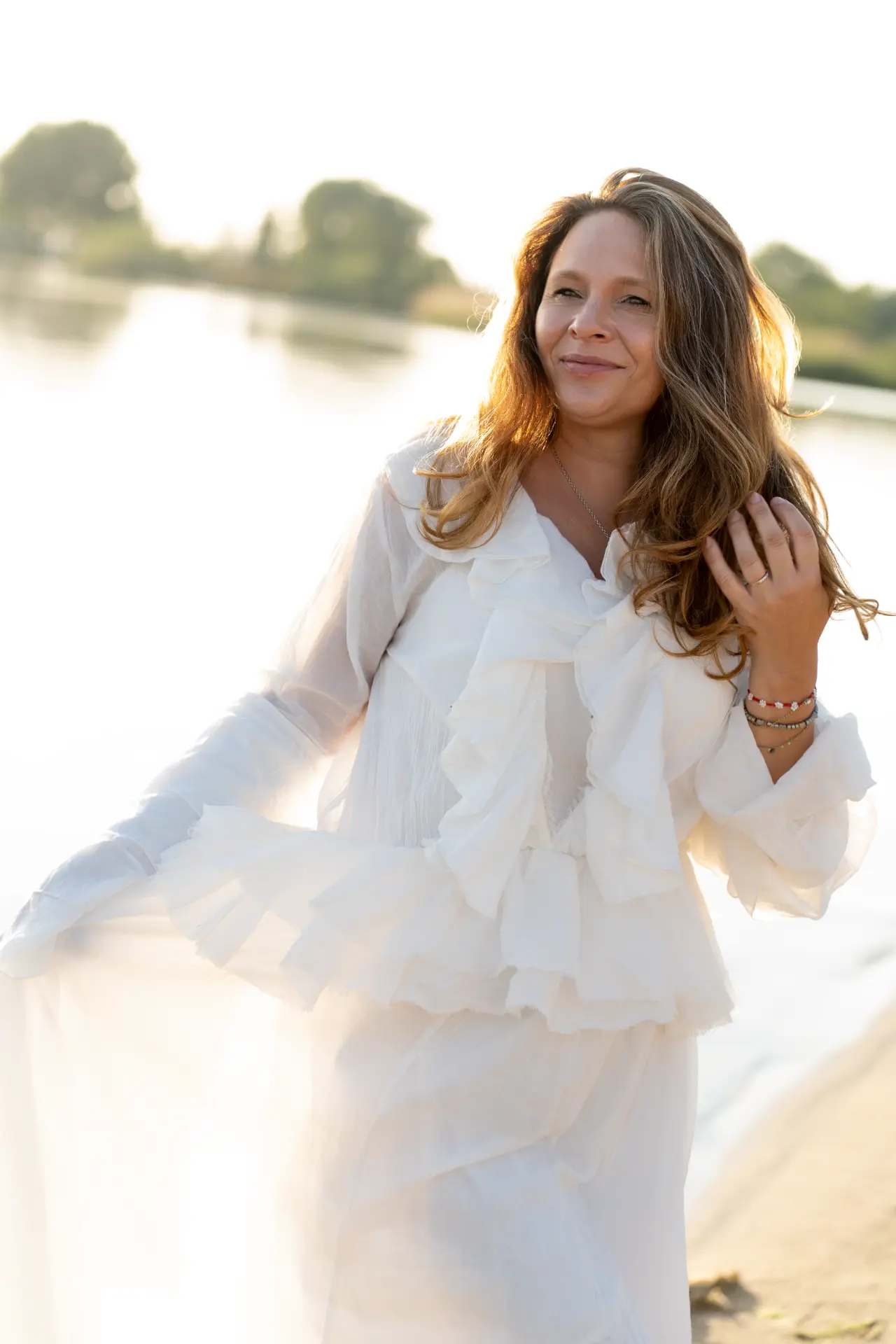 Woman in a white ruffled dress by a river at golden hour