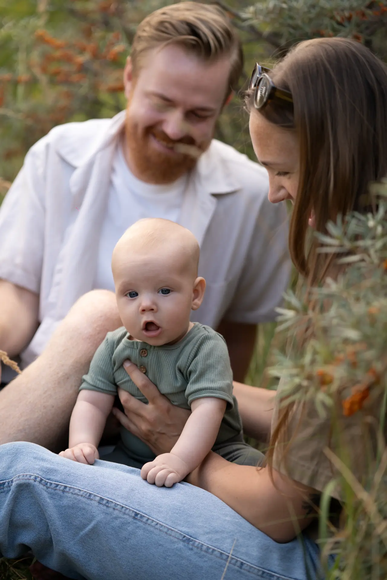 Parents watching their baby among sea buckthorn branches