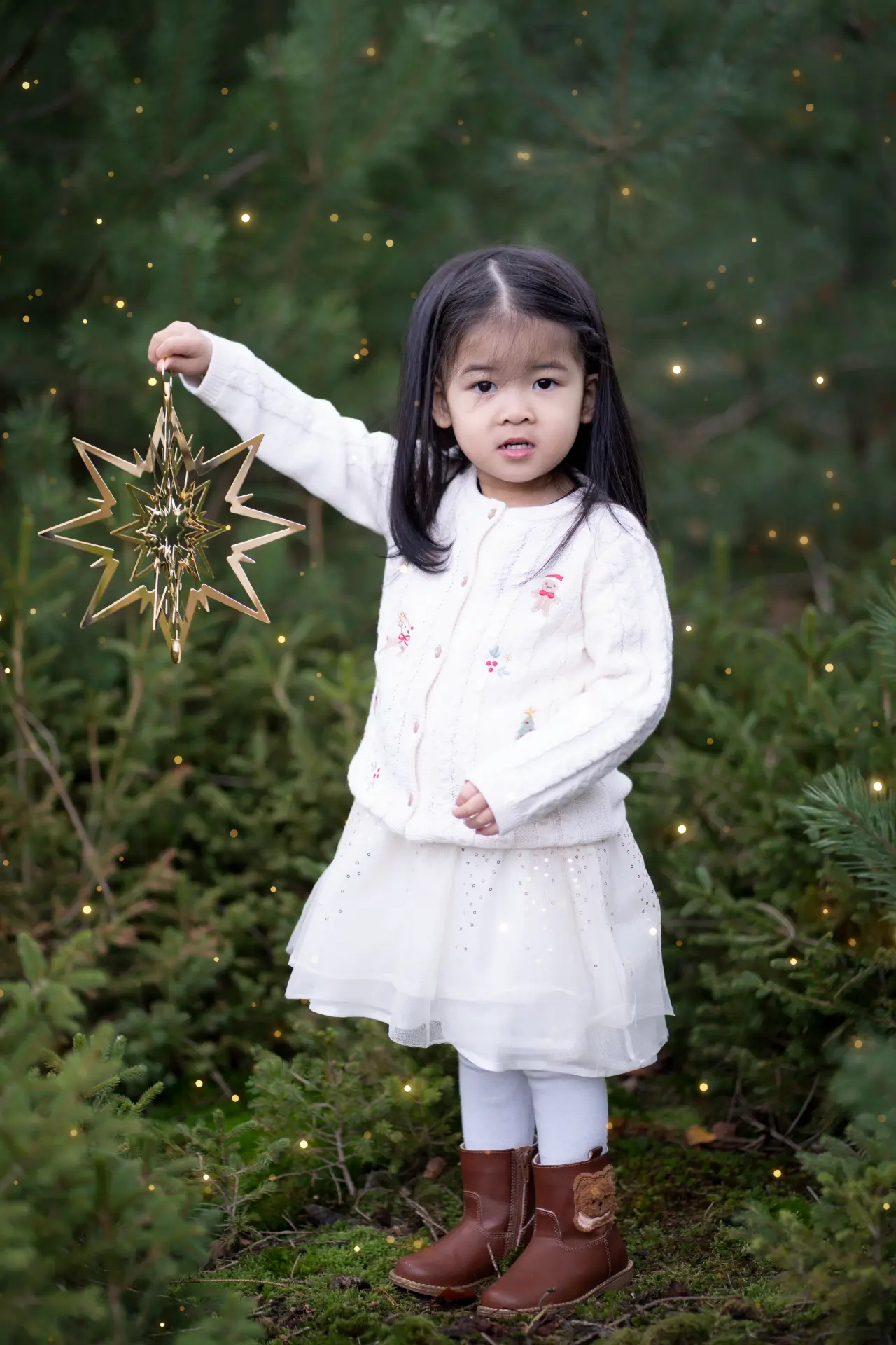 Little girl holding a golden star ornament among the pines