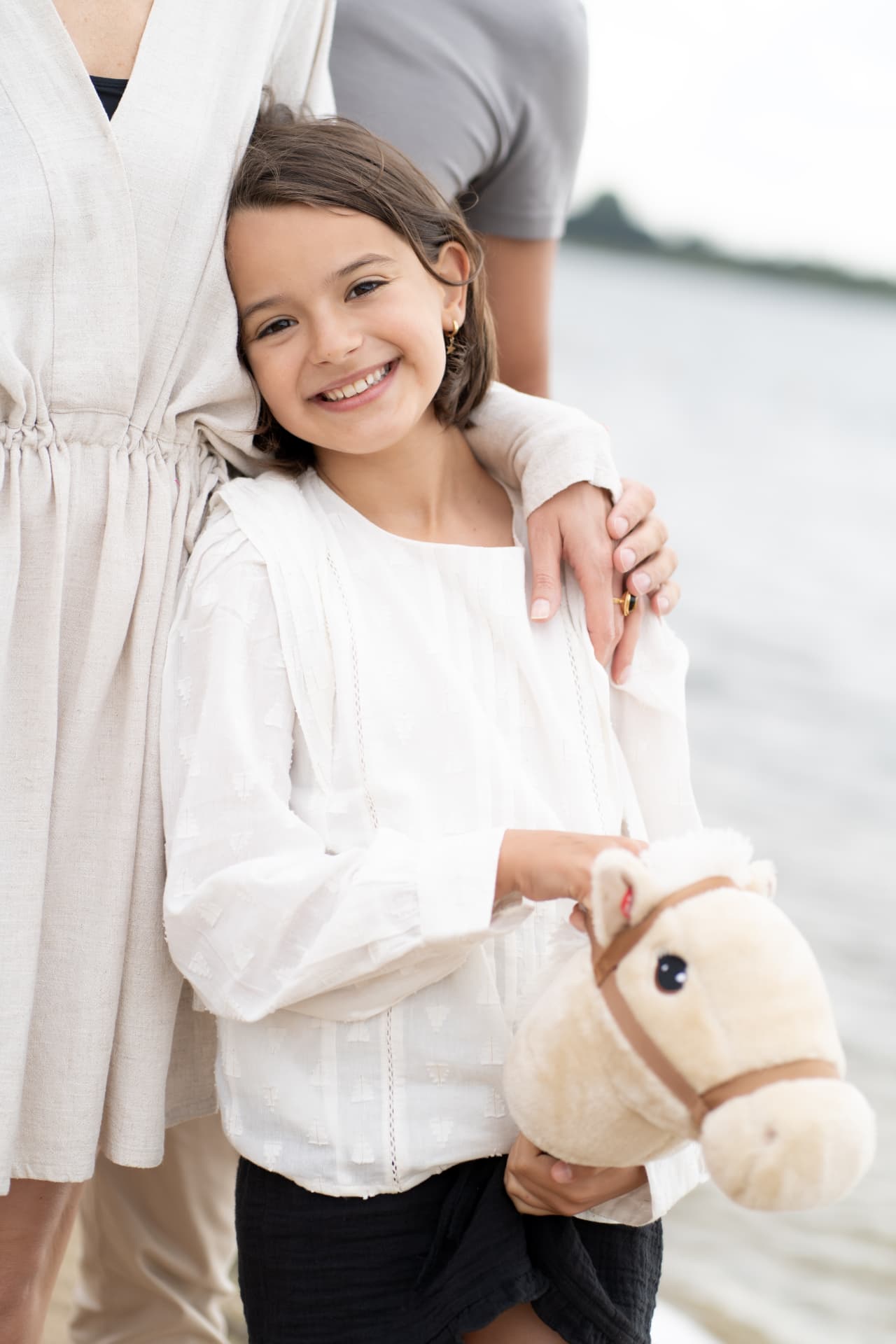 Girl holding a toy horse beside her mother at the shore